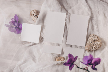 Wedding invitation mockup with orchid, papers on white textile background. Top view, flat lay. Wedding stationary. Perfect for presentation of your invitation, menu, greeting cards