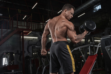 Muscular athletic bodybuilder man hard workout in gym over dark background with dramatic light with barbell