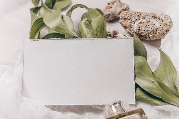 Wedding invitation mockup with paper, stone, green branch on white textile background. Top view, flat lay. Wedding stationary. Perfect for presentation of your wedding invitation, menu, greeting cards