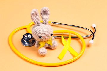 Wall Mural - Children's toy with a Childhood Cancer Awareness Golden Ribbon and stethoscope on yellow background.