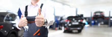 Focus On Hand Of Happy Engineer Man Showing Thumb Up And Standing In Modern Car Maintenance Garage With Automobiles. Machinery Repairman Concept. Blurred Background
