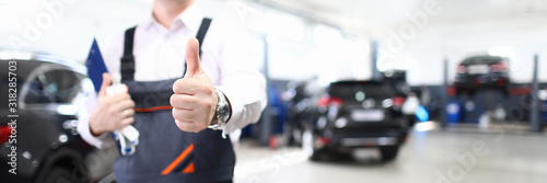 Fotomural Focus on hand of happy engineer man showing thumb up and standing in modern car maintenance garage with automobiles