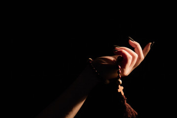 Wall Mural - Close-up young female hand holding rosary beads for praying. Black isolated background.