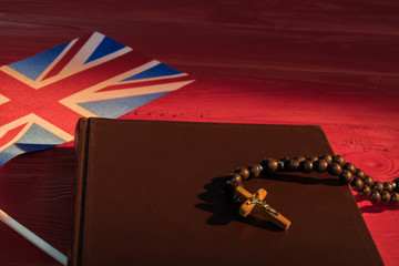 Wall Mural - Great Britain catholicism concept. Rosary with crucifix, holy bible and flag of UK, red wood background.