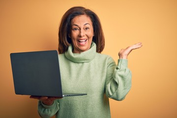 Middle age brunette woman using computer laptop over yellow background very happy and excited, winner expression celebrating victory screaming with big smile and raised hands