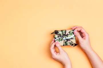 Wall Mural - Female hands holding a gift box with khaki ribbon on a yellow background.