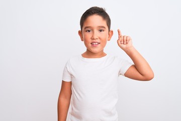 Wall Mural - Beautiful kid boy wearing casual t-shirt standing over isolated white background showing and pointing up with finger number one while smiling confident and happy.