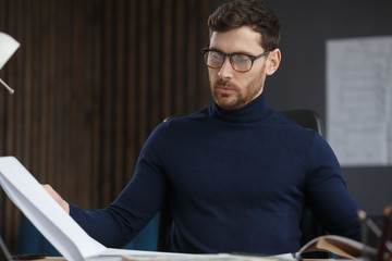 Wall Mural - Architect working in office with blueprints.Engineer inspect architectural plan, sketching a construction project.Portrait of handsome bearded man sitting at workplace. Business construction concept.
