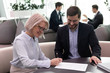 © fizkes - Happy young businessman watching smiling mature businesswoman signing agreement.