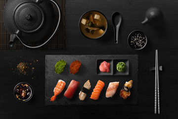 Sushi rolls, sashimi set, miso soup and teapot, on dark wooden table, Japanese food, top view.