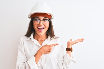 Canvas Print - Young beautiful architect woman wearing helmet and glasses over isolated white background amazed and smiling to the camera while presenting with hand and pointing with finger.