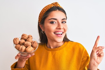 Sticker - Young beautiful woman holding bowl with walnuts standing over isolated white background very happy pointing with hand and finger to the side