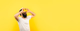 Fototapeta  - bearded hipster man holding lemon slices in front of eyes, over yellow background, panoramic mock-up with space for text