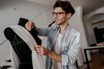 Wall Mural - Male fashion designer, creative designer of designer clothes smiles and folds fabric on a mannequin. Design, studio for sewing and cutting clothes, designer clothes, manufacturing, craft product.
