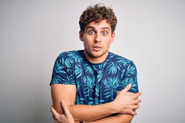 Young blond handsome man on vacation with curly hair wearing casual summer t-shirt shaking and freezing for winter cold with sad and shock expression on face