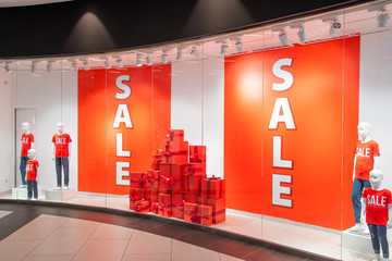 Huge red signs with information about the sale in the shop window. Near manikins and gift boxes. Promotion, advertising, shopping and black friday concept