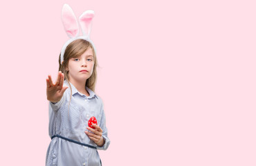 Sticker - Young blonde child wearing easter bunny ears with open hand doing stop sign with serious and confident expression, defense gesture