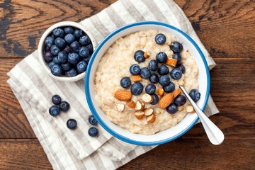 Blueberry almond oatmeal porridge in bowl on a wooden table background, top view. Healthy food, clean eating concept