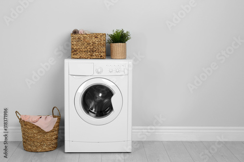 Fotomural Modern washing machine with houseplant and laundry baskets near white wall