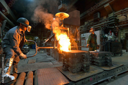 Fotomural workers in a foundry casting a metal workpiece - safety at work and teamwork