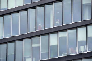 Glass transparent facade of a modern office building made of individual rectangular elements. Behind the glass you can see office chairs and tables