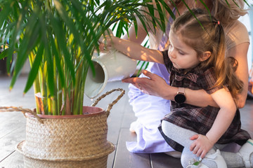 Little toddler girl watering plants with her mother in home. Making domestic work