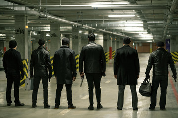 Rear view of row of criminals or gangsters in black standing on parking area