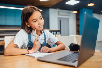 Pretty girl using a laptop computer for homework at modern blue classroom.