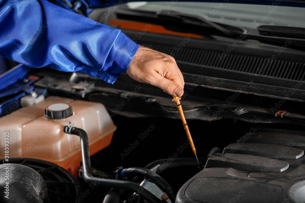 Male mechanic checking level of oil in car engine