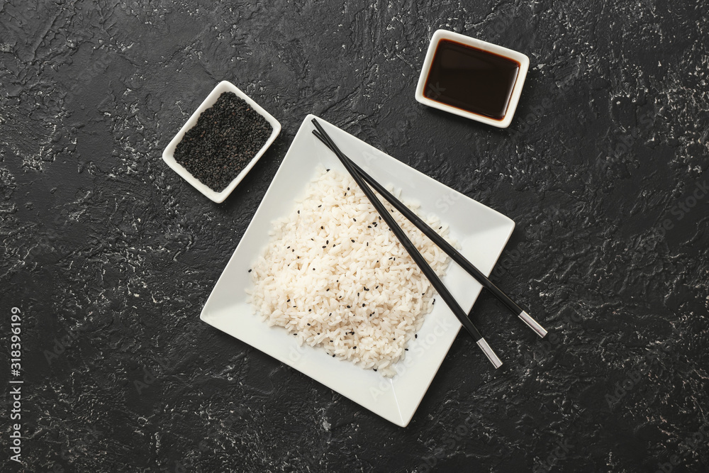 Plate with boiled rice and soy sauce on dark background