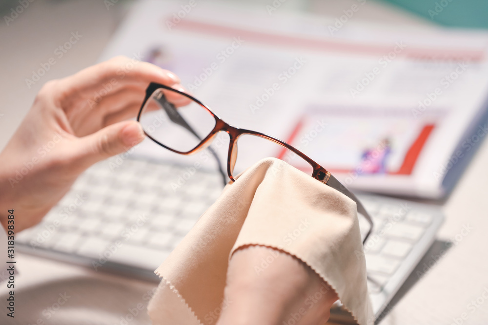 Young woman wiping eyeglasses at table, closeup