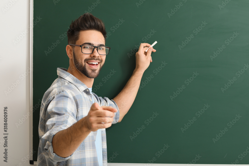 Male teacher writing on blackboard in classroom - obrazy, fototapety, plakaty 
