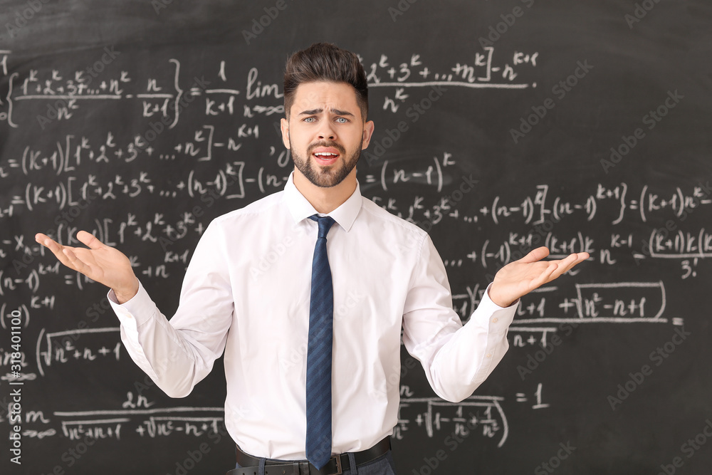 Confused male teacher near blackboard in classroom