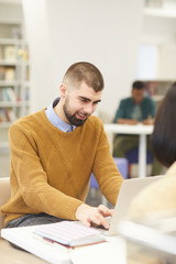 Wall Mural - Portrait of smiling young man using laptop while studying in college library with other people in background, copy space