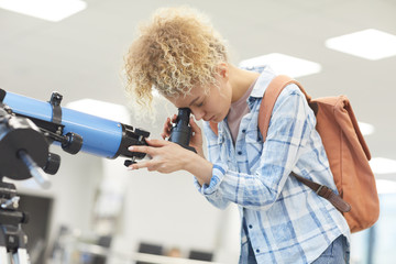 side view portrait of funky female student looking into telescope in college library, copy space