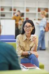 Wall Mural - Portrait of smiling Asian student wearing glasses discussing project with partner while sitting at table in college library, copy space