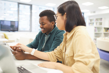 Wall Mural - Portrait of two students studying in college library, focus on Asian young woman using laptop in foreground
