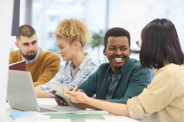 Wall Mural - Multi-ethnic group of students studying in college library, focus on African-American man smiling at partner