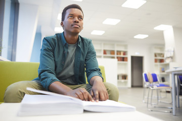 Wall Mural - Portrait of young African-American man reading braille while studying in school library, copy space