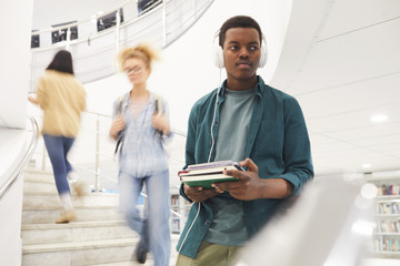 Wall Mural - Waist up portrait of African-American student holding books while going down spiral stairs in modern college interior, copy space