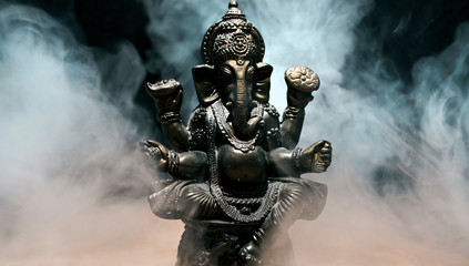 Hindu god Ganesha on black background. Statue with a smoke of incense. 