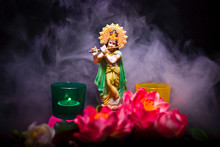 Hindu God Krishna. Statue With A Smoke And Lotus Flowers On A Black Background