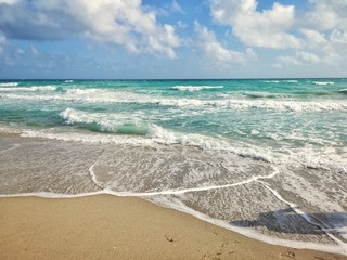 Beautiful blue aquamarine colour sea ocean water landscape with white foam. Seascape nature with waves, blue sky and sandy beach at bright sunny summer day. Natural wallpaper and background texture.