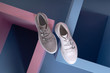 white and gray female sneakers with fasteners on buttons, shoes of the same model stand on a pink, blue stand from the studio. Promotional photo