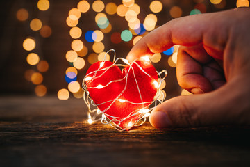 Wall Mural - Holding a red heart shape covered with led lights on wooden and bokeh lights background. Valentines day and romance concept.