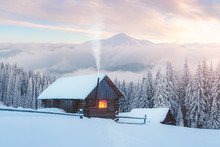 Fantastic Winter Landscape With Wooden House In Snowy Mountains. Smoke Comes From The Chimney Of Snow Covered Hut. Christmas Holiday And Winter Vacations Concept