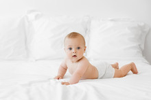 Side View Of Cute Baby Lying On Belly On White Bed