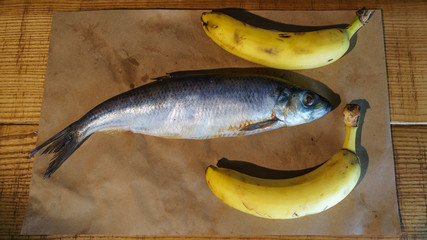 Close-up delicious salted herring and two yellow bananas on the old wooden background. Rustic style.