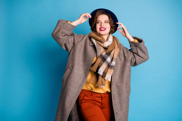 Poster - Photo of traveler lady toothy smiling good mood sunny day weather wear stylish casual long grey coat yellow pullover orange pants hat isolated blue color background