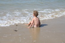 Rear View Of Shirtless Boy Sitting On Shore At Beach